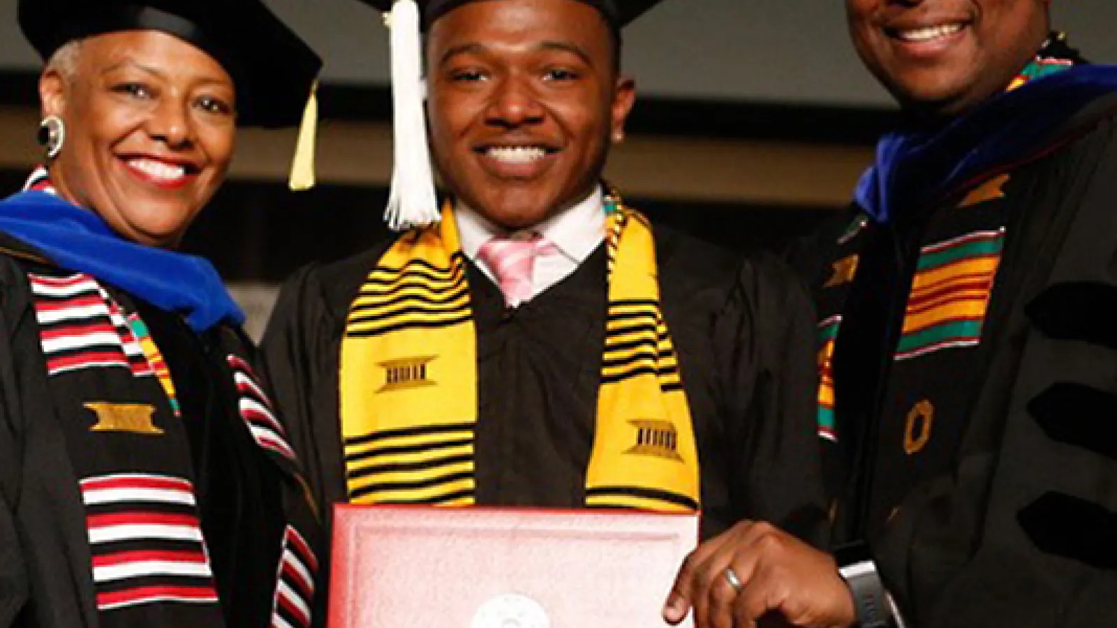 Undergraduate student wearing graduation cap and down standing with his advisors